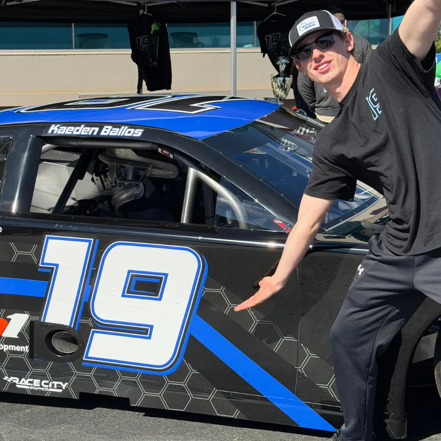 Kaeden Ballos beside the #19 Late Model, helmet raised, preparing for the next race.