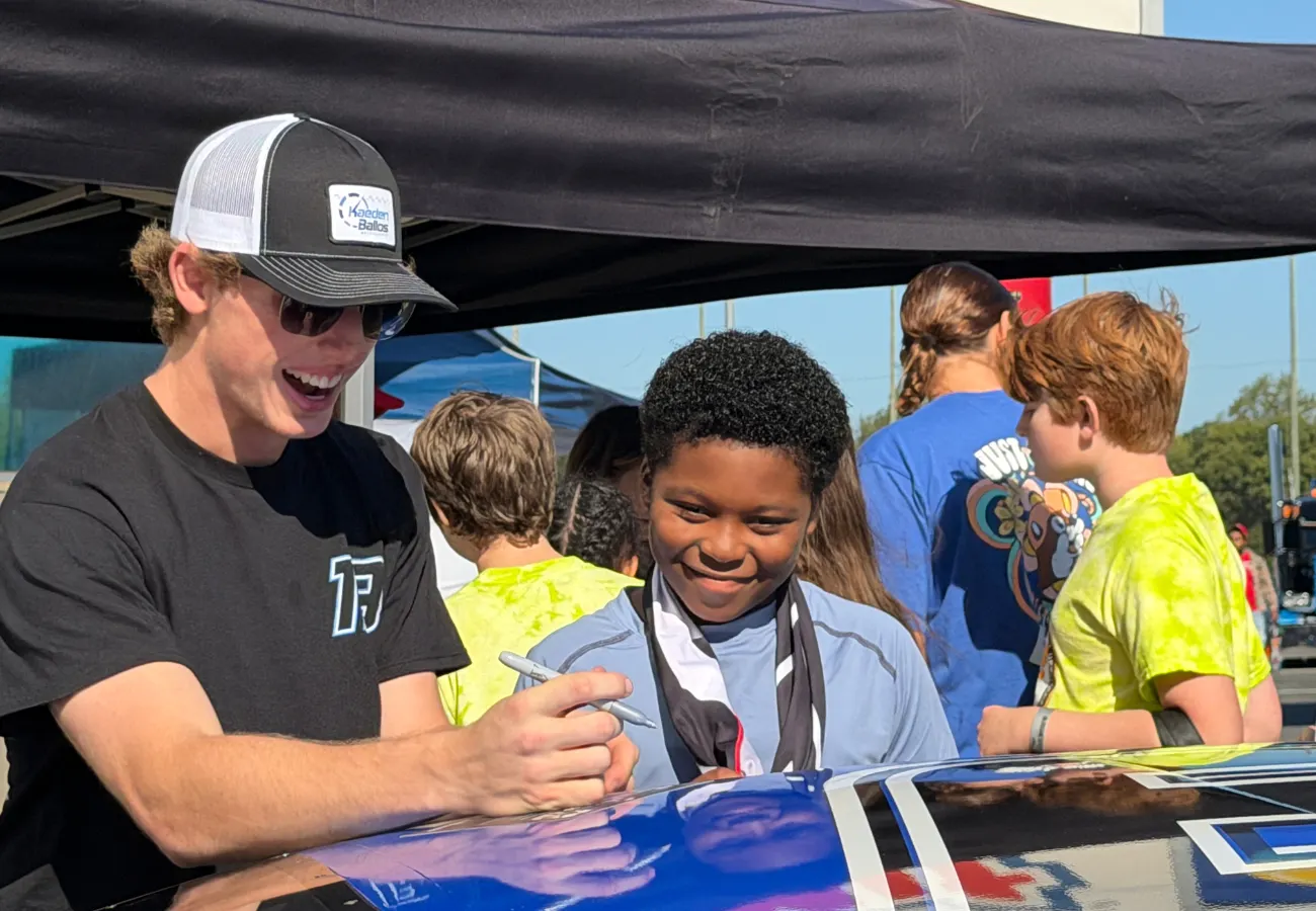 Students and families at a STEAM Expo with hands-on science activities and a Kaeden Ballos Motorsports race car display.